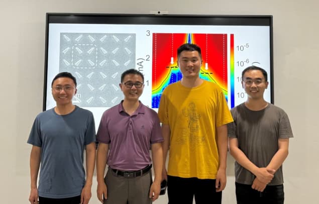 Photo of four members of the research team, standing in front of a diagram showing the arrangement of the crystalline material used in this research