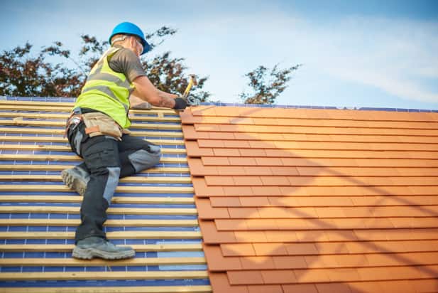 a roofer nails on roof tiles