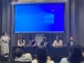 Photo of the moderator and five panellists in front of a blue backdrop