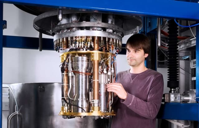 Christof Gaiser standing next to a complicated set of metal tubes and wires suspended from the ceiling to a