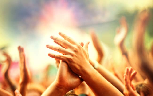 Large group of people holding their arms and hands high in the air during an outdoor concert